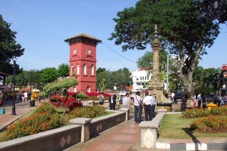 Gezellige stadsplein met de rode klokkentoren, diverse mensen, groene bomen en kleurrijke bloemen in Penang, Maleisië, populair toeristenmijdpunt met historische architectuur en levendige sfeer.