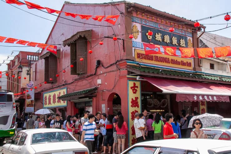 Kleurrijk Chinees-Maleis restaurant met rij wachtende klanten, traditionele decoraties en straatverlichting, gelegen in een levendige omgeving in Kuala Lumpur, Maleisië.