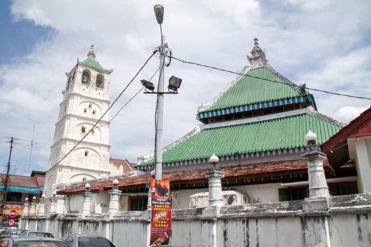 Kleurrijke Chinese tempel met groene dakpannen en een hoge witte toren in een stedelijke omgeving in Maleisië.