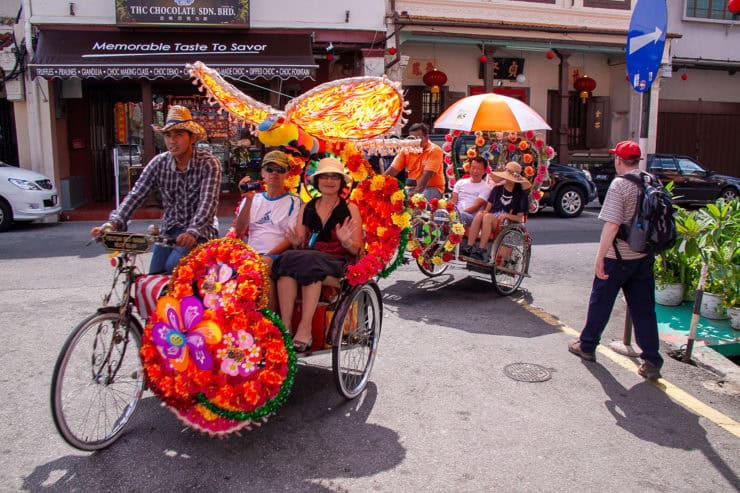 Kleurrijke voertuig met bloemenversiering tijdens straatparade in Maleisië, toeristen genieten van levendige festivale sfeer.