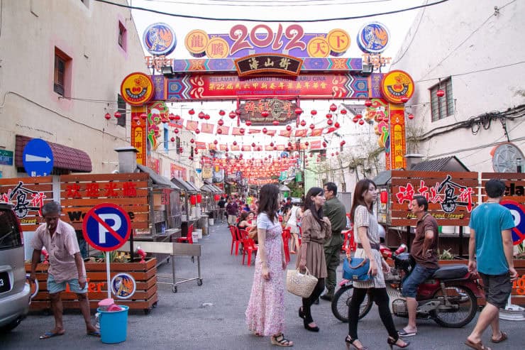 Verschillende mensen wandelen en zitten op straat in een Chinese nieuwjaarsviering met rode decoraties en lampionnen in een gezellige straatmarkt.