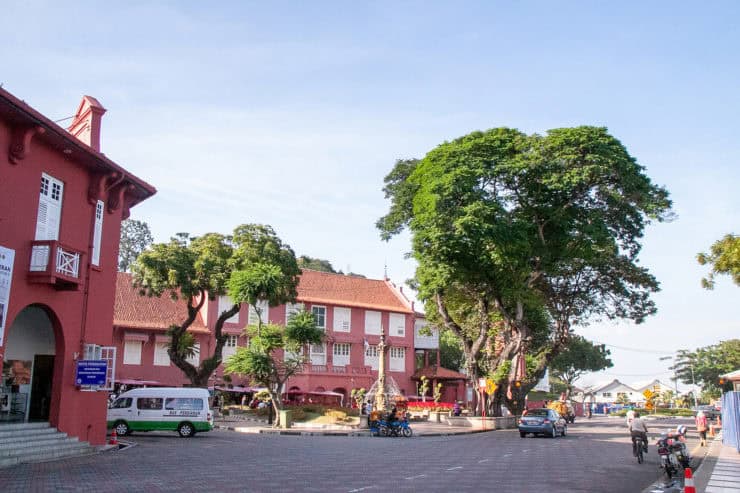 Kleurrijke gebouwen en groene bomen in een rustige straat in Maleisië, met een standbeeld in het midden en een heldere blauwe lucht.