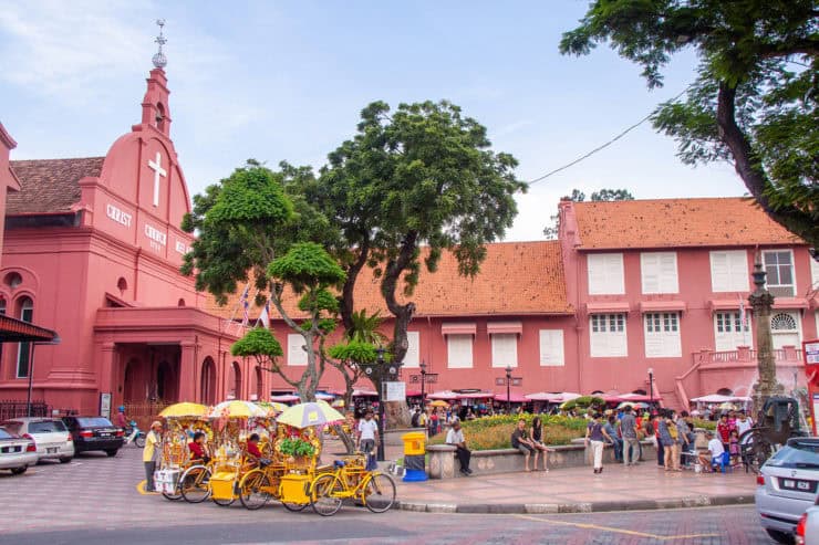 Kleurrig straatbeeld met historische kerktoren, mensen en fiets-taxi's in George Town, Penang, Maleisië, typisch voor toeristische attracties en cultuur.