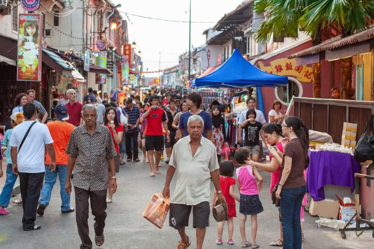 Kleurrijke straatmarkt in Maleisië met diverse mensen, souvenirs en eetkraampjes onder Chinese decoraties, typische sfeer van culturele verscheidenheid en levendigheid.