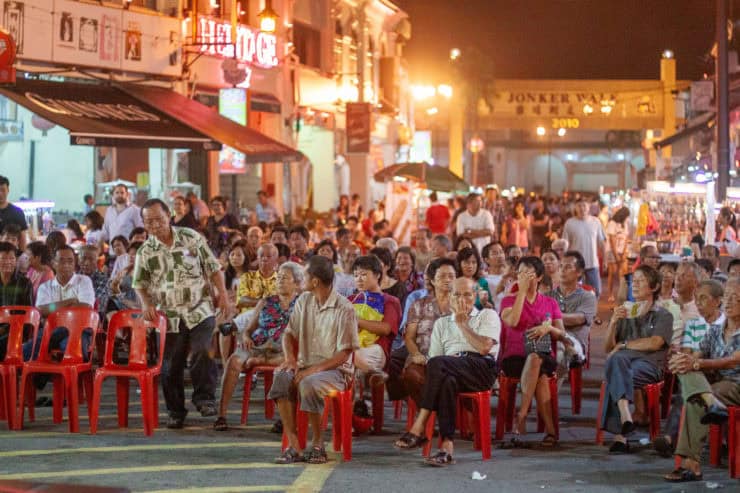 Gezellige mensen bij een avondmarkt in Maleisië met kleurrijke lichten, straatkraampjes en een levendige sfeer.