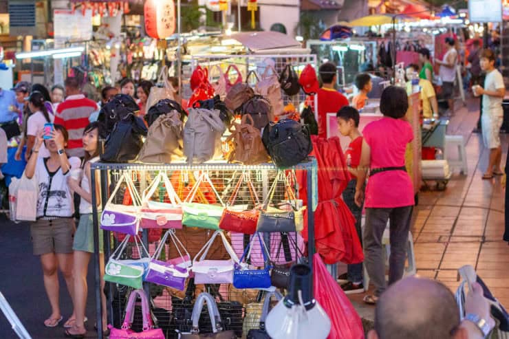 Handelaren verkoopt kleurrijke tassen en backpacks op een levendige avondmarkt in Maleisië.