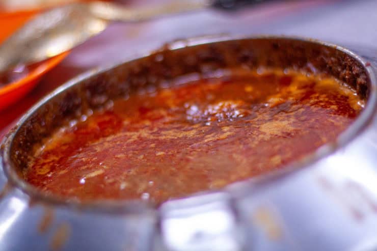 Sappige rode curry in een metalen pan met rijke saus, typisch voor Maleisische keuken, klaar om geserveerd te worden.