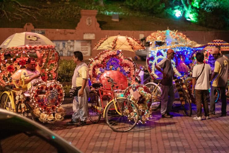 Versierde fietstaxi's met bloemen en verlichting tijdens een avondmarkt in Maleisië, benadrukt de kleurrijke cultuur en levendige straatcultuur van het land.