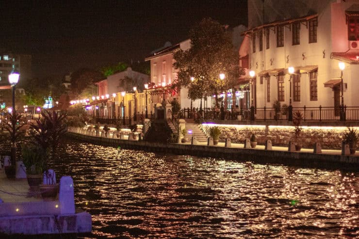 Kleurrijke nachtzicht van een verlichte rivierpromenade met historische gebouwen en straatverlichting in Maleisië, perfect voor het promoten van diversiteit en cultuur toerisme.