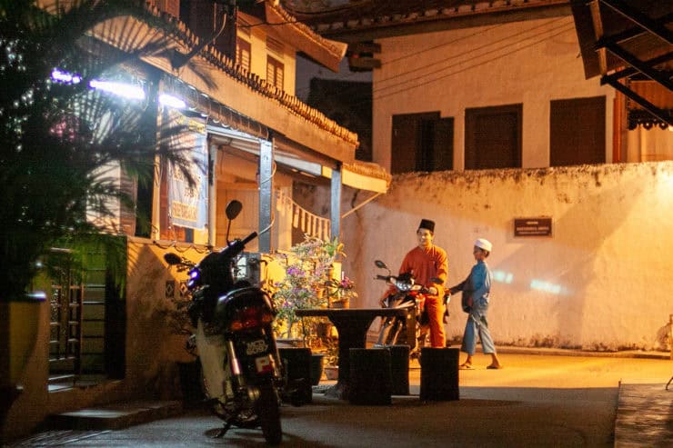 Kleurrijk straatbeeld in Maleisië met lokale bewoners op een avond, traditionele kleding en motorfietsen, sfeervol verlicht en authentiek stadsleven.