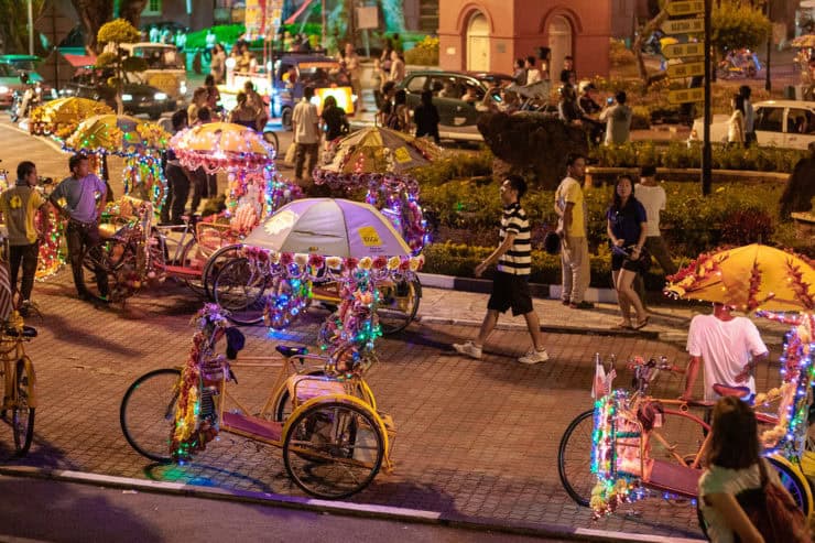 Kleurrijke fietstaxi's met versierde parasols op straat tijdens avond in Maleisië, levendige sfeer, toeristen en locals genieten van de drukke stad.